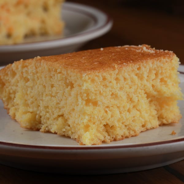 A golden-brown slice of Arizona BBQ Shack cornbread on a white plate with a brown rim.
