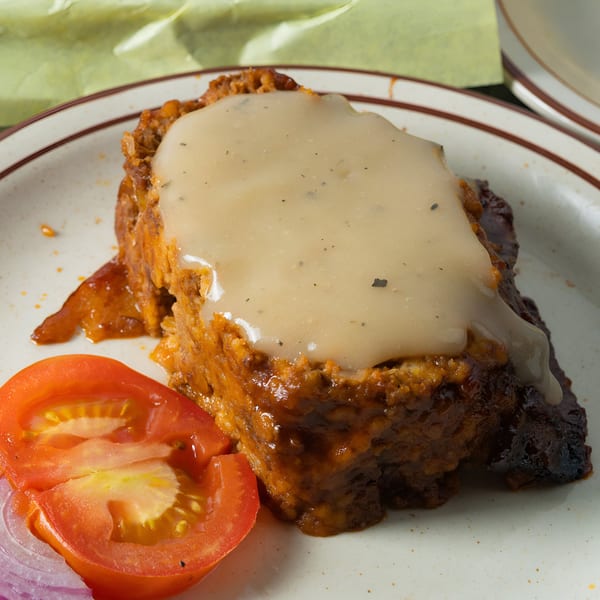 Arizona BBQ Shack's meatloaf with gravy, sliced tomatoes, and red onions on a white plate.