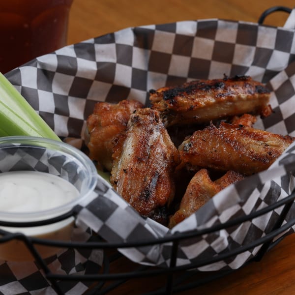 Grilled chicken wings in a checkered basket with celery sticks and ranch dressing.