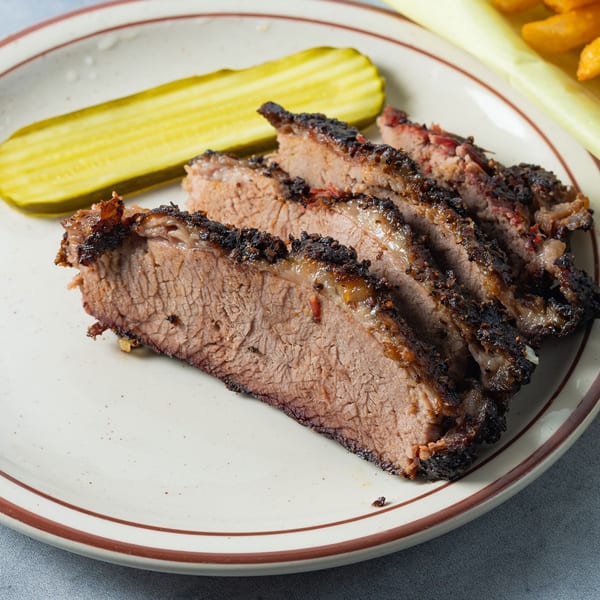 Slices of Arizona BBQ Shack's brisket with a dark crust and a side of pickle on a plate.