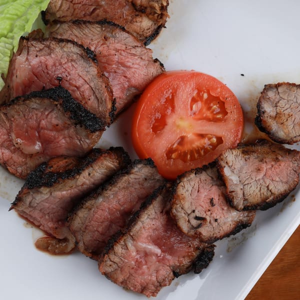 Slices of medium-rare barbecued meat with a charred crust, served with a tomato slice and lettuce.