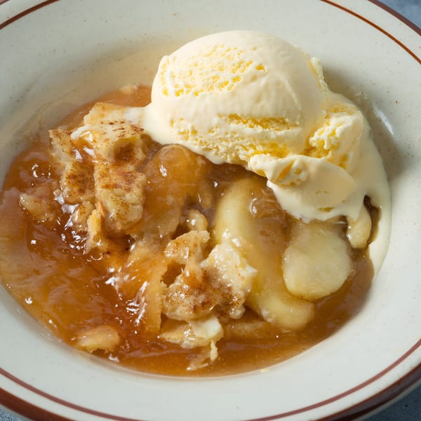 Warm apple cobbler with a scoop of vanilla ice cream in a white bowl with brown rim.