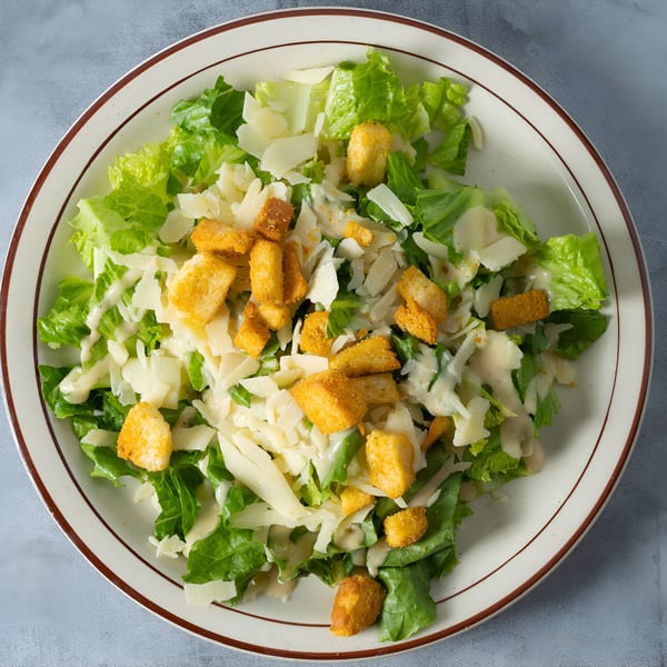 Caesar salad with romaine lettuce, parmesan cheese, croutons, and dressing on a white plate.