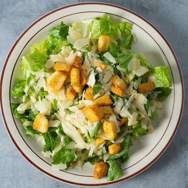 Caesar salad with romaine lettuce, parmesan cheese, croutons, and dressing on a white plate.