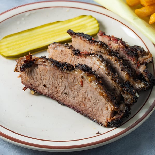 Slices of Arizona BBQ Shack brisket with a dark, crispy bark and a pickle spear on a plate.