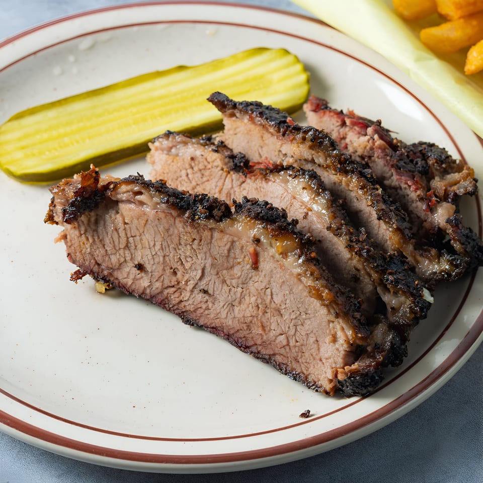 Slices of Arizona BBQ Shack brisket with a dark, crispy bark and a pickle spear on a plate.
