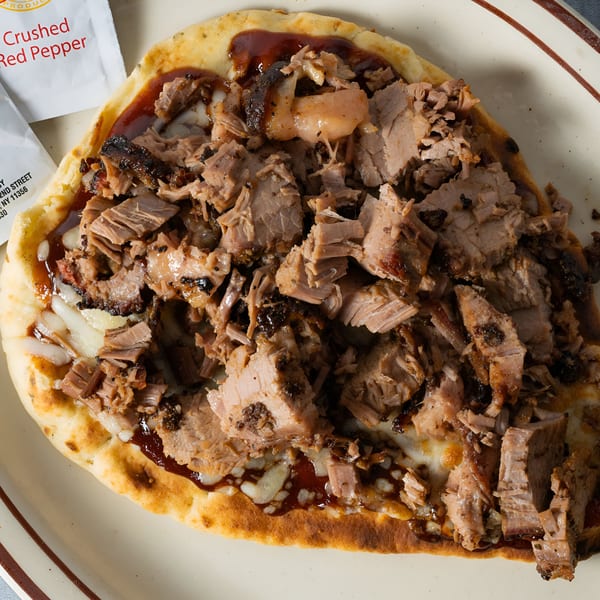 Close-up of a BBQ flatbread pizza with shredded meat, melted cheese, and barbecue sauce.