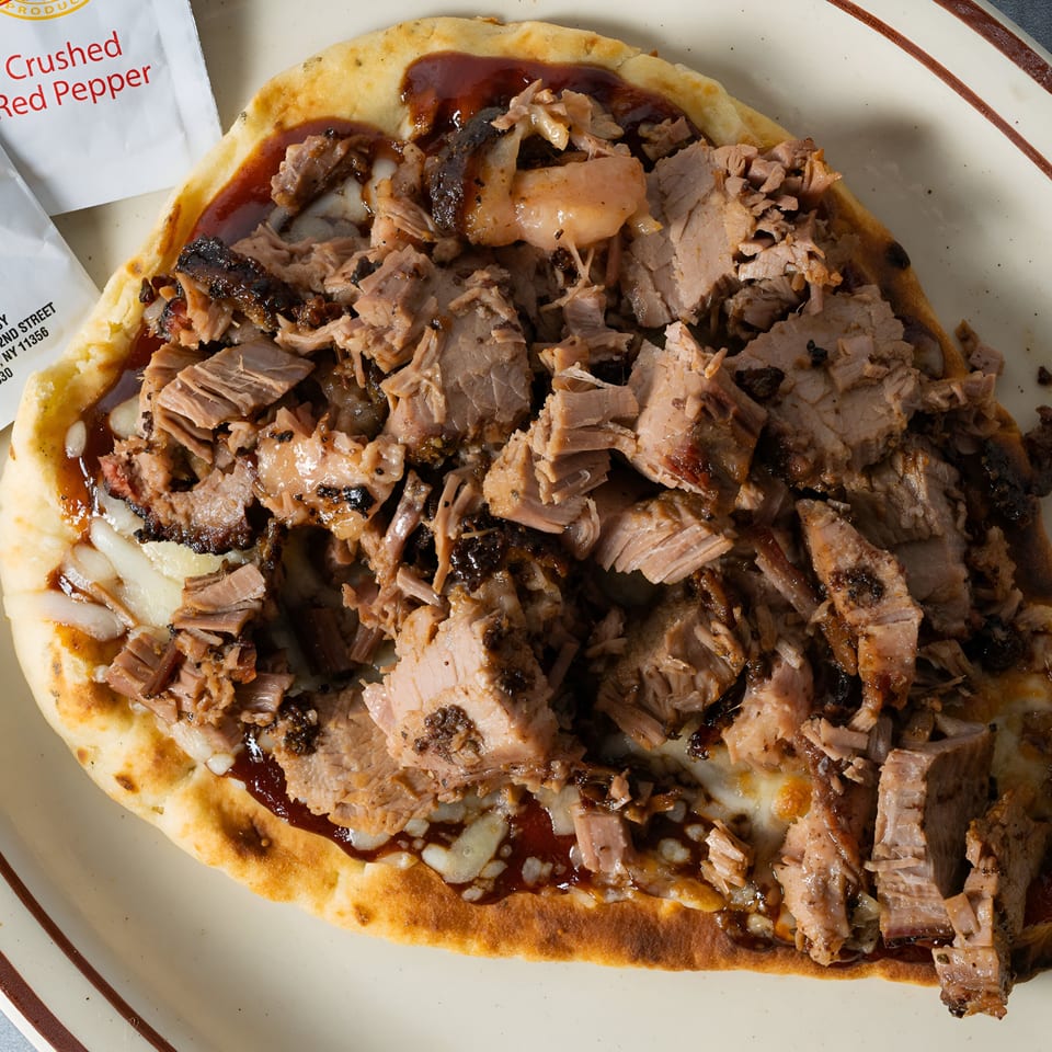Close-up of a BBQ flatbread pizza with shredded meat, melted cheese, and barbecue sauce.