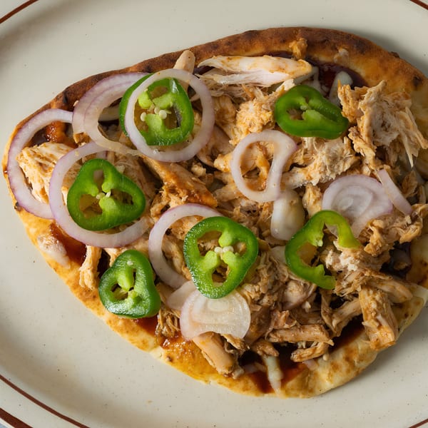 Arizona BBQ Shack's flatbread with shredded chicken, red onion, and sliced jalapeños on a white plate.